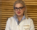 Person wearing a white coat with a visible logo against a wooden panel background