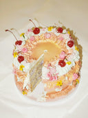 Decorative cake with whipped cream, cherries, and flowers on a white plate.