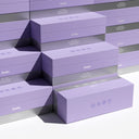 Stacked lavender and gray Amíu boxes arranged in a geometric display on a white background.